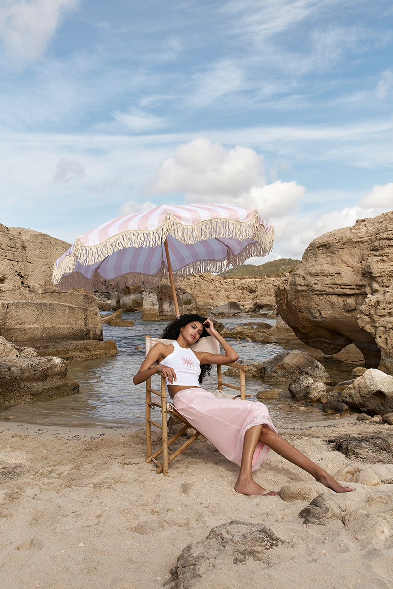 Ikinita Sunrise Top, a stylish women’s blouse in vibrant sunrise colors, shown on a hanger with floral background.