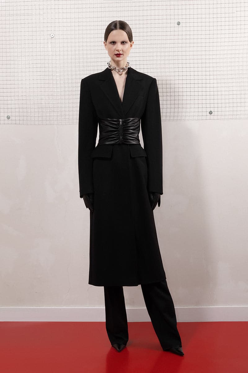Black Vaska vegan leather coat with belt, tailored fit, featuring long sleeves and classic style, shown in size XS.