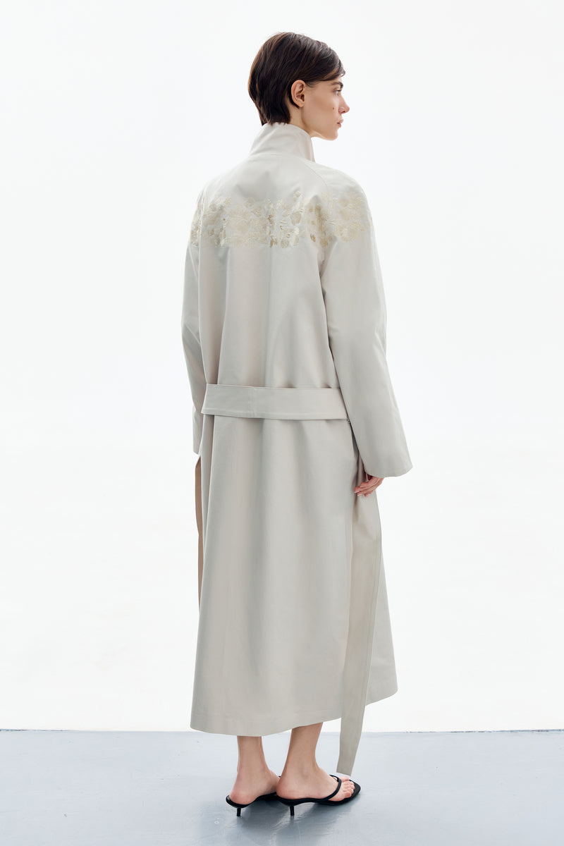 Back view of a beige PETAL GREY BEIGE trench coat by DELEGAN, showing classic collar and stylish belted design.