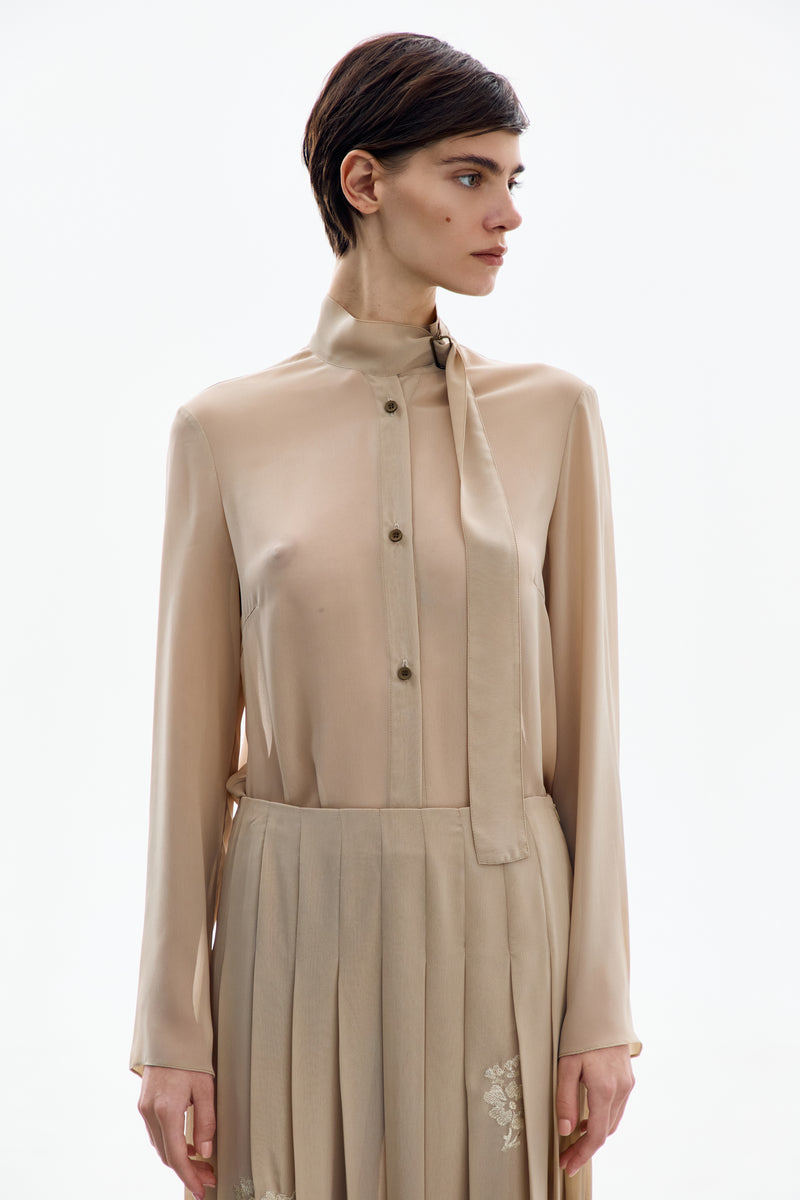 Front view of a nude gold long sleeve blouse by DELEGAN, featuring a sleek design and fitted style.