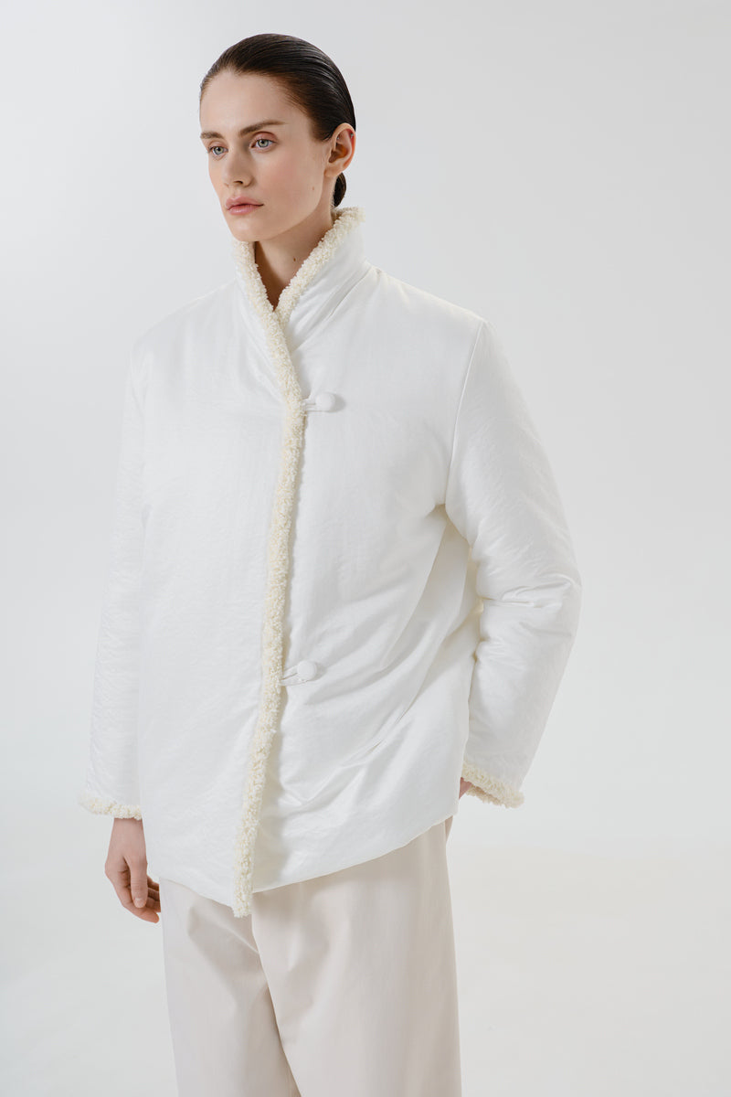 White DELEGAN jacket worn side view showing front zipper, collar, and long sleeves on a neutral background.