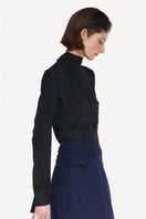 Black tie neck blouse by DELEGAN, stylish shirt with a bow tie detail, worn side view showing fabric and design details.