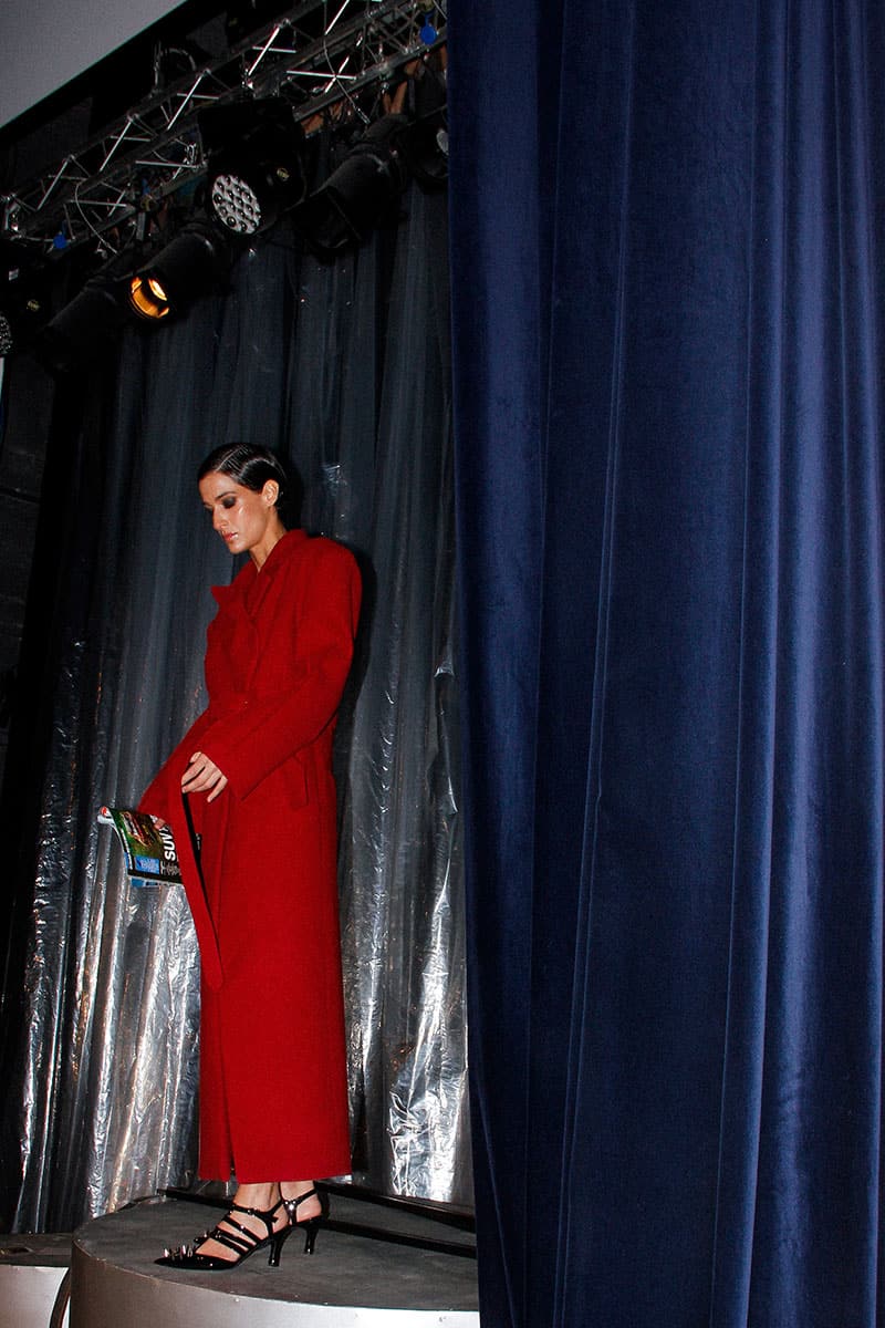 Full-length maroon coat by Blikvanger featuring a structured design, shown on a model with a high collar and tailored fit.