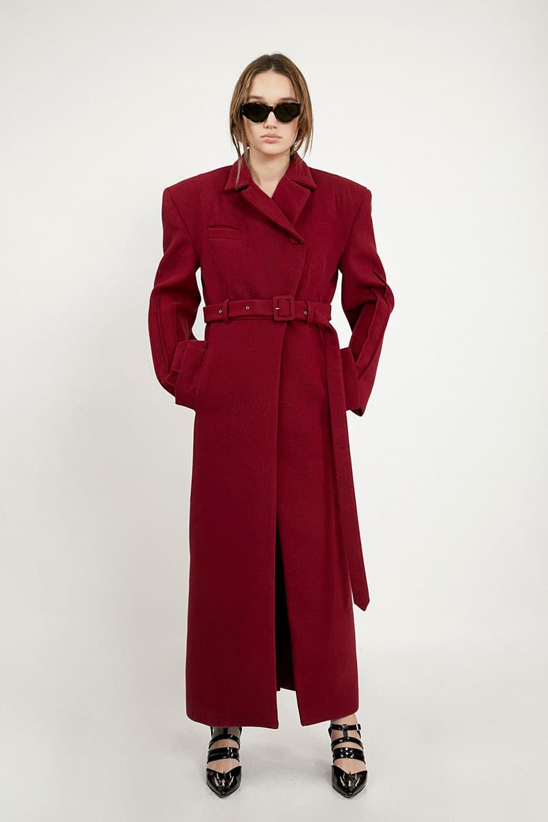 Full-length maroon coat by Blikvanger, structured design, shown hanging with front view and detailed fabric texture.