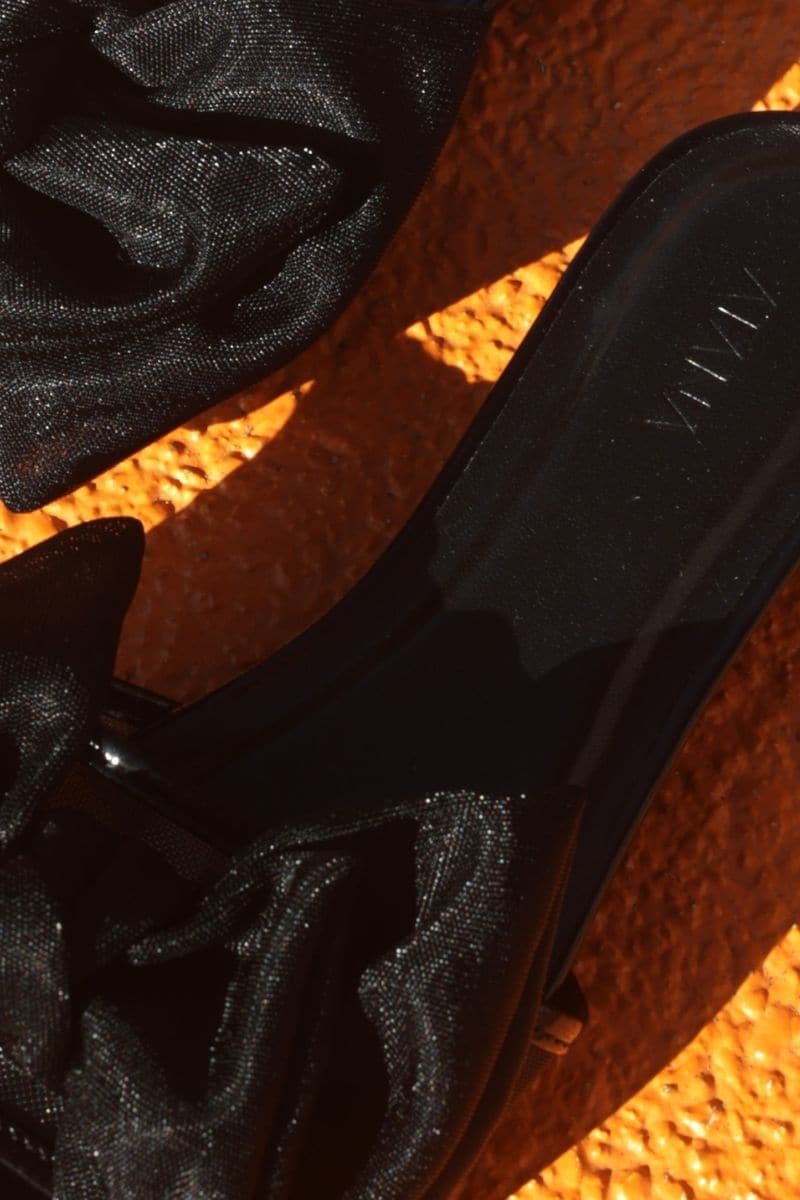 Black patent bow sliders by House of Atana, stylish flat sandals with a prominent bow detail on the straps.
