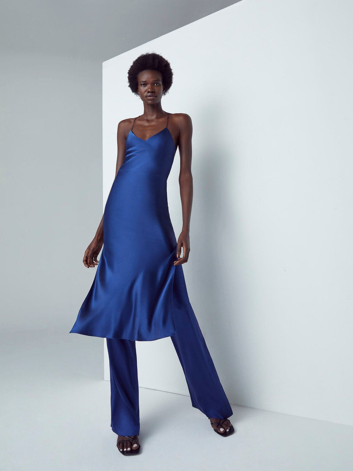Silked sapphire silk midi slip dress hanging on a white background, showcasing its sleek and elegant design.