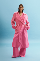 Vaska belted hot pink trench coat displayed on a hanger, showcasing its vibrant color and classic design.