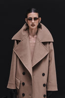 Vaska double-breasted relaxed coat in caramel color, shown on a model, with a tailored fit and classic lapel design.